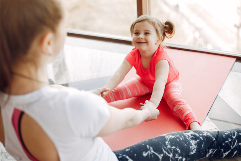 Woman in a sportswear. Mother with little daughter. Family are engaged in gymnastics in a gym